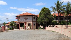 A hotel with a red-tiled roof, a covered entrance, and a gravel driveway. - Hotel Karina (Itapetininga)