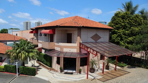 A two-story building with a red-tiled roof, a covered entrance, and a small outdoor seating area. - Hotel Karina (Itapetininga)