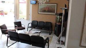 A waiting area with black leather chairs, a coffee table with magazines, a chandelier, a television, and a framed floral painting on the wall. - Hotel Karina (Itapetininga)