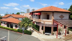A hotel with a red-tiled roof, a covered entrance, and a small outdoor seating area with chairs and potted plants. - Hotel Karina (Itapetininga)