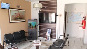 A waiting area with a TV, framed artwork, a chandelier, and a fire extinguisher. - Hotel Karina (Itapetininga)