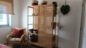 Una habitación con una estantería de madera, un sillón de mimbre y una planta verde grande.