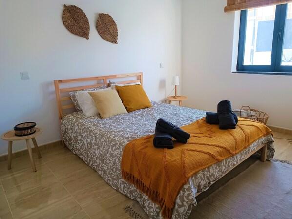 A neatly arranged bedroom with a bed, bedside tables, a small round table, and a window with blinds.