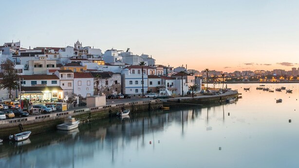 Un pueblo costero con edificios a lo largo de un muelle, barcos amarrados y un mar tranquilo.