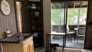 A kitchen with wooden cabinets, a countertop, and a dining area with a table and chairs. - Cozy Cabin on Cobbossee Lake near Lakeside Marina (Winthrop)