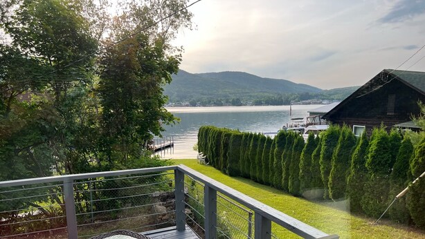 Una terraza con mesa y sillas de cristal, con vista a un lago y una zona boscosa.