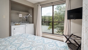 A bedroom with a bed, a washing machine, a dryer, and a window with a view of trees. - Kiwanie Lodge, Large Lakefront Home, Sleeps 12 (Hardy)