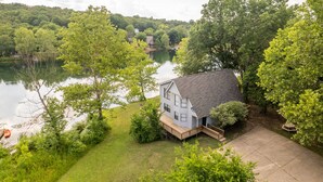 A house with a deck overlooking a lake, surrounded by trees and greenery. - Kiwanie Lodge, Large Lakefront Home, Sleeps 12 (Hardy)
