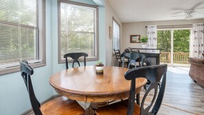 A dining area with a wooden table and chairs, large windows with blinds, a ceiling fan, and a view of the outdoors. - Kiwanie Lodge, Large Lakefront Home, Sleeps 12 (Hardy)
