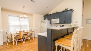 A compact kitchen with a microwave, refrigerator, and a small island. There is a dining area with wooden chairs and a table. - 2 Britt Buoys - Oceanfront 4BR duplex, (Surf City)