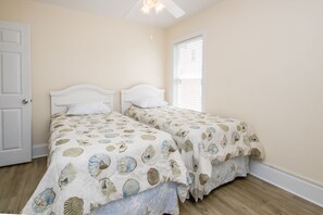 A bedroom with two single beds, a ceiling fan, a window with blinds, and a door.
