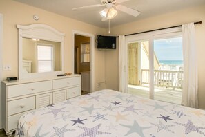 A bedroom with a bed, dresser, television, and a balcony with a view of the beach. - 2 Britt Buoys - Oceanfront 4BR duplex, (Surf City)