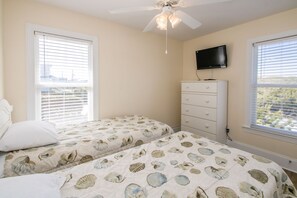 A bedroom with two beds, a ceiling fan, a dresser, and a TV on the wall.