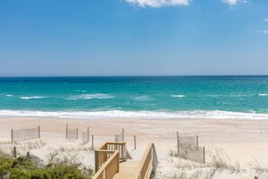 A beach with a wooden boardwalk leading to the water, sandy dunes, and a clear blue sky.