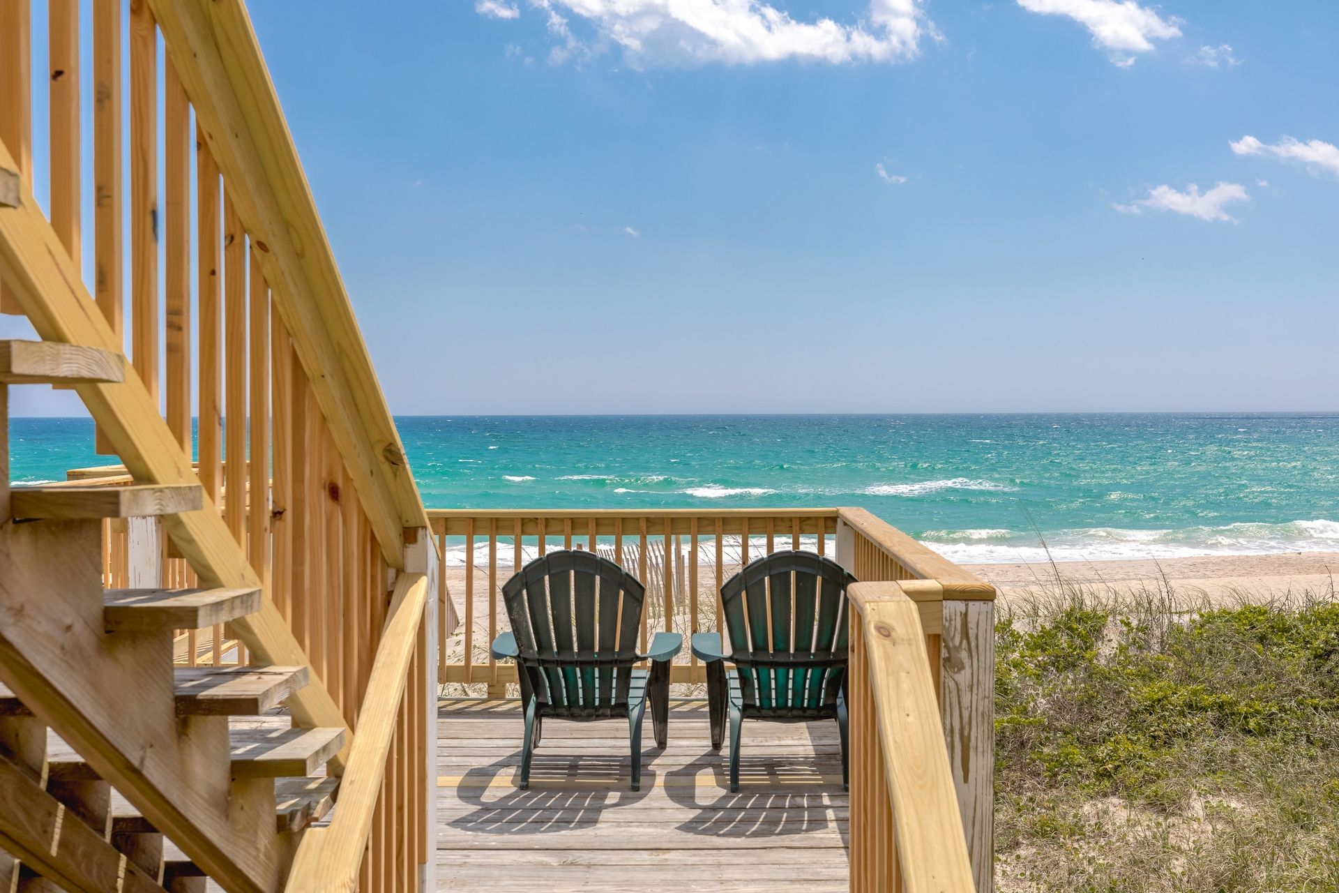 A wooden deck with two chairs facing the ocean.