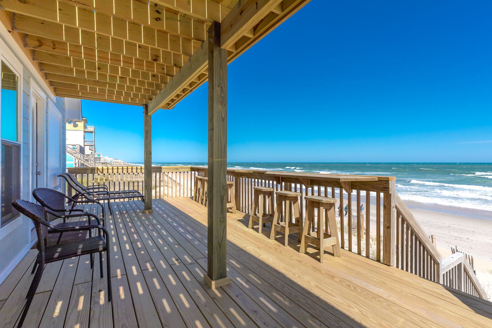 Una terraza de madera con sillas, con vista a una playa y olas.