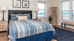 A bedroom with a bed, bedside tables, a window with a view, and a door. - Beach Barn Lower - Lovely 3BR Lower Unit on the Oceanfront (Surf City)