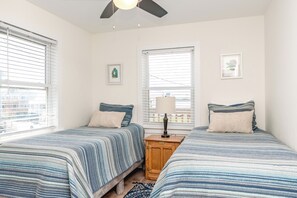 A bedroom with two beds, a nightstand, a ceiling fan, and two windows with blinds. - Beach Barn Lower - Lovely 3BR Lower Unit on the Oceanfront (Surf City)