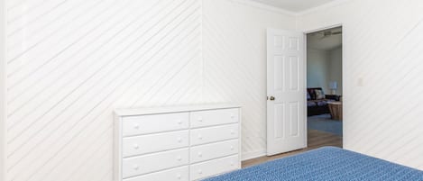 A bedroom with a bed, a dresser, and a door leading to another room.