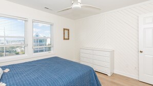 A bedroom with a bed, a white dresser, a ceiling fan, and a window with blinds.