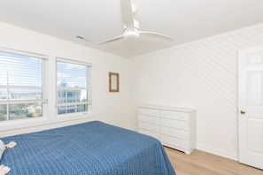 Un dormitorio con cama, tocador blanco, ventilador de techo y ventana con persianas.