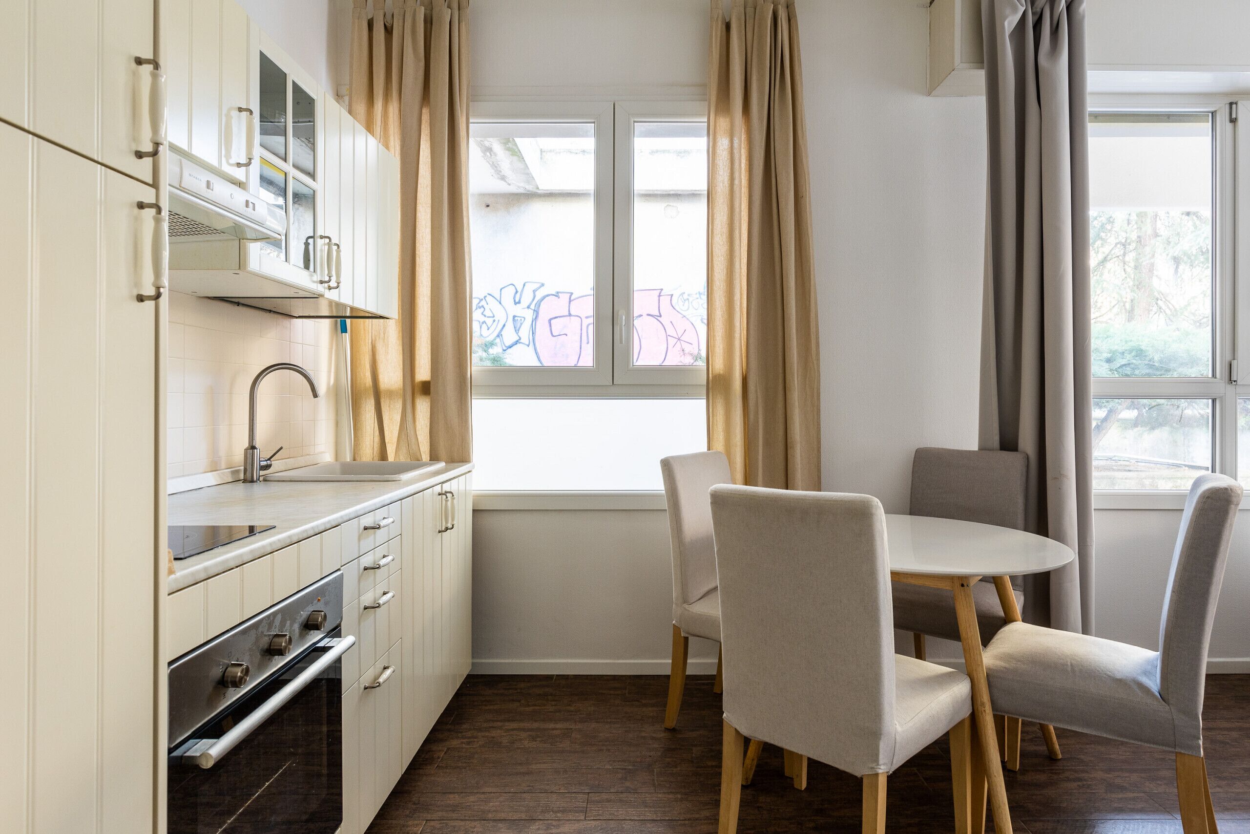 Una cocina moderna con armarios blancos, horno integrado y una ventana con cortinas.