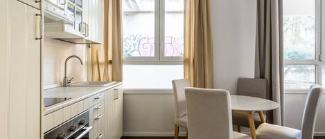 Una cocina moderna con armarios blancos, horno integrado y una ventana con cortinas.