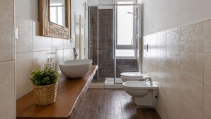 Une salle de bain moderne avec un meuble-lavabo en bois, un grand lavabo sur pied, un bidet et une douche à parois de verre.
