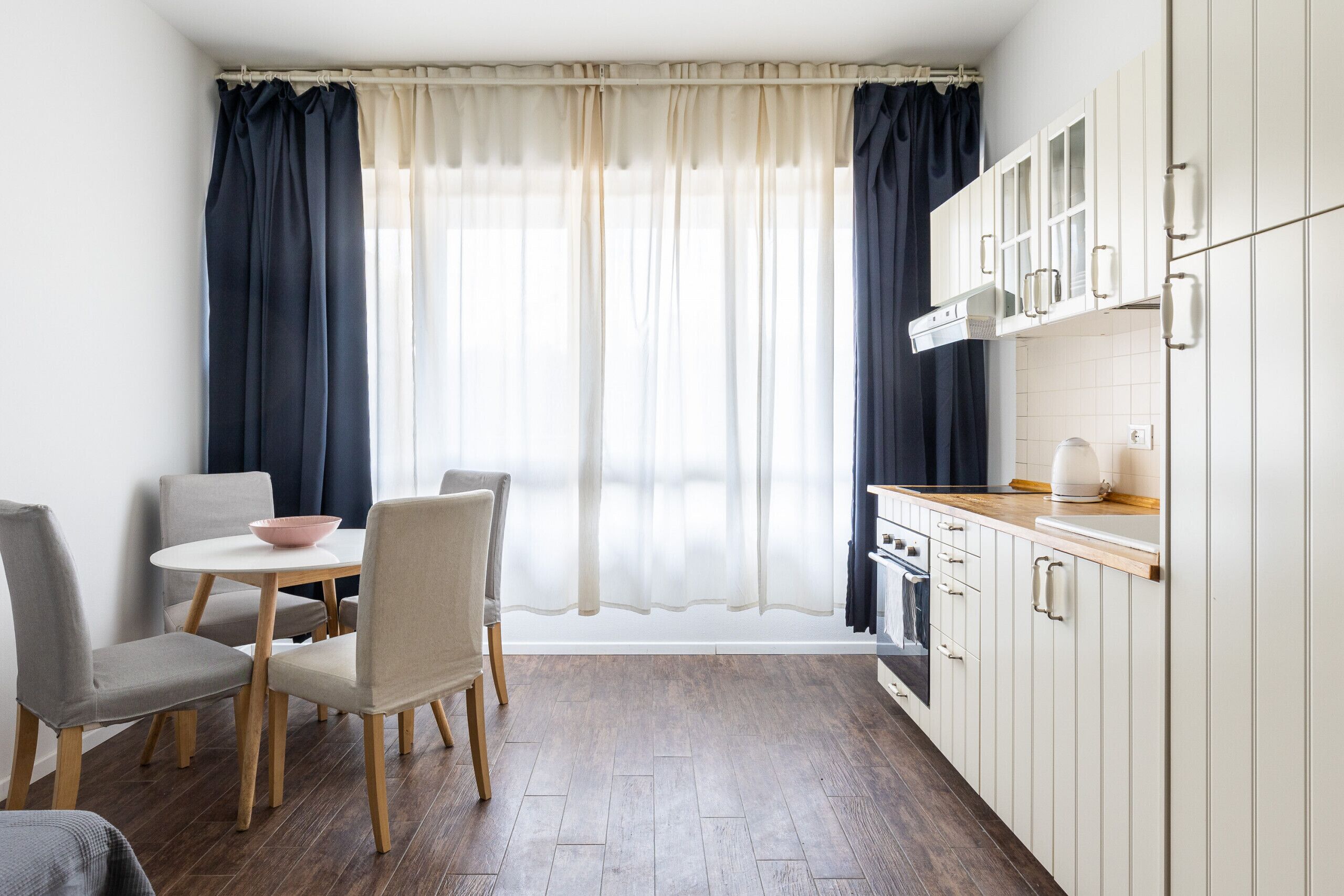 Een moderne keuken met witte kasten, een houten aanrecht en een eethoek met een ronde tafel en stoelen.