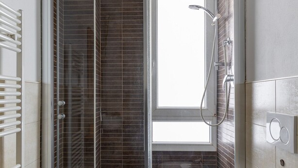 Une salle de bain moderne avec une douche à parois de verre, des toilettes blanches et une fenêtre laissant entrer la lumière naturelle.