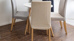 Un coin repas avec une table ronde et quatre chaises, une œuvre d’art représentant une porte bleue au mur, et une fenêtre avec des rideaux foncés.