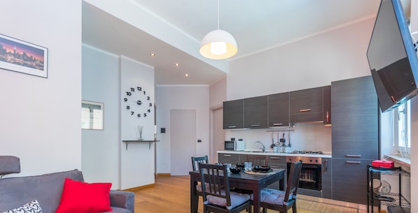 Een modern appartement met een eethoek, keuken en woonkamer met een bank en rode kussens.