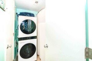A laundry room with two stacked washing machines and a door. - @ Seas The Day - Charming 1BR Surf Condo; Community Pool (Surf City)