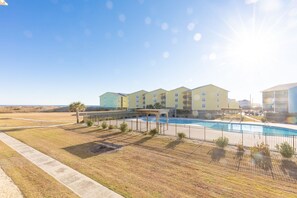 A hotel with a swimming pool, multiple-story buildings, and a clear sky. - @ Seas The Day - Charming 1BR Surf Condo; Community Pool (Surf City)
