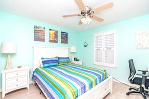 A bedroom with a bed, nightstands, a desk, and a ceiling fan.