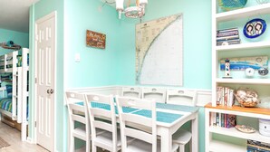 Una habitación con paredes verde azulado, una puerta blanca, un mapa en la pared y una estantería con libros y objetos decorativos.