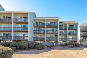 A multi-story hotel with balconies, a pool area, and a well-maintained lawn. - Sun And Surf - Top Floor 2 BR Surf Condo - Community Pool (Surf City)
