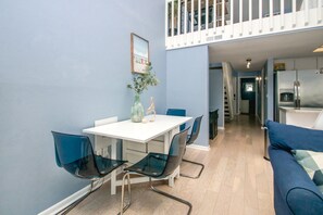 A dining area with a white table and blue chairs, a vase with greenery, and a staircase leading to a balcony.