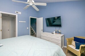 Un dormitorio con cama, cómoda, televisor, ventilador de techo, silla de mimbre y una escalera.