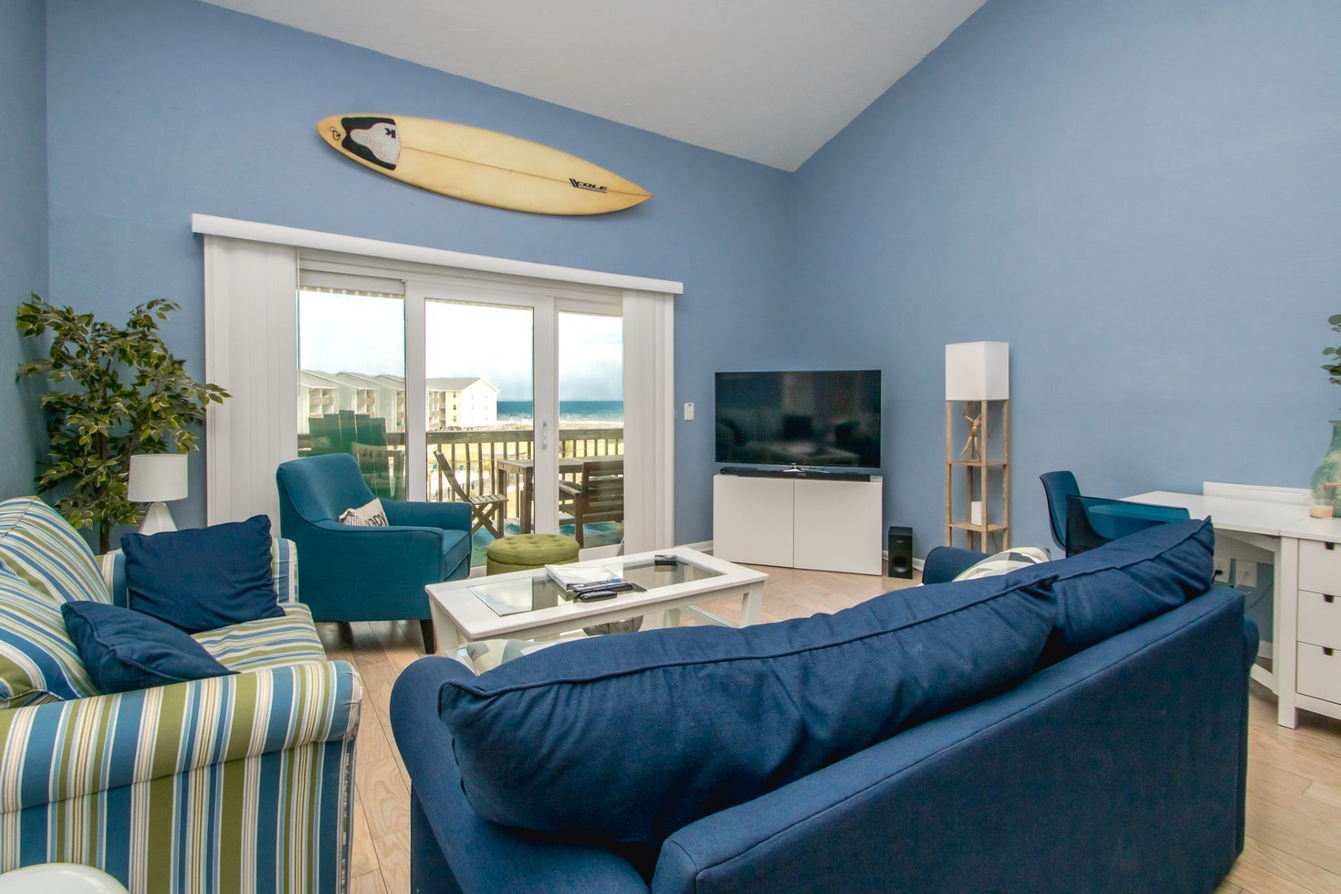 A living room with a large window, a television, a surfboard, and a plant.