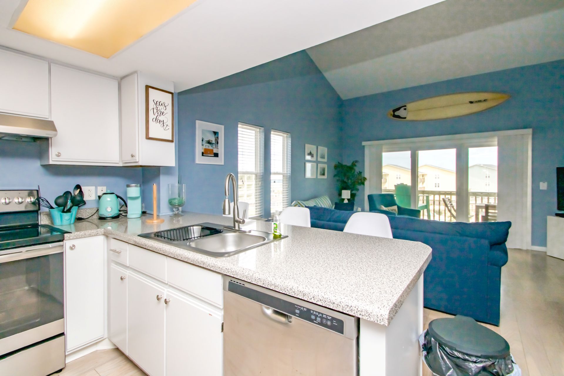 Una cocina moderna con lavavajillas, un lavamanos doble y un comedor con sofá azul y decoración de tabla de surf.