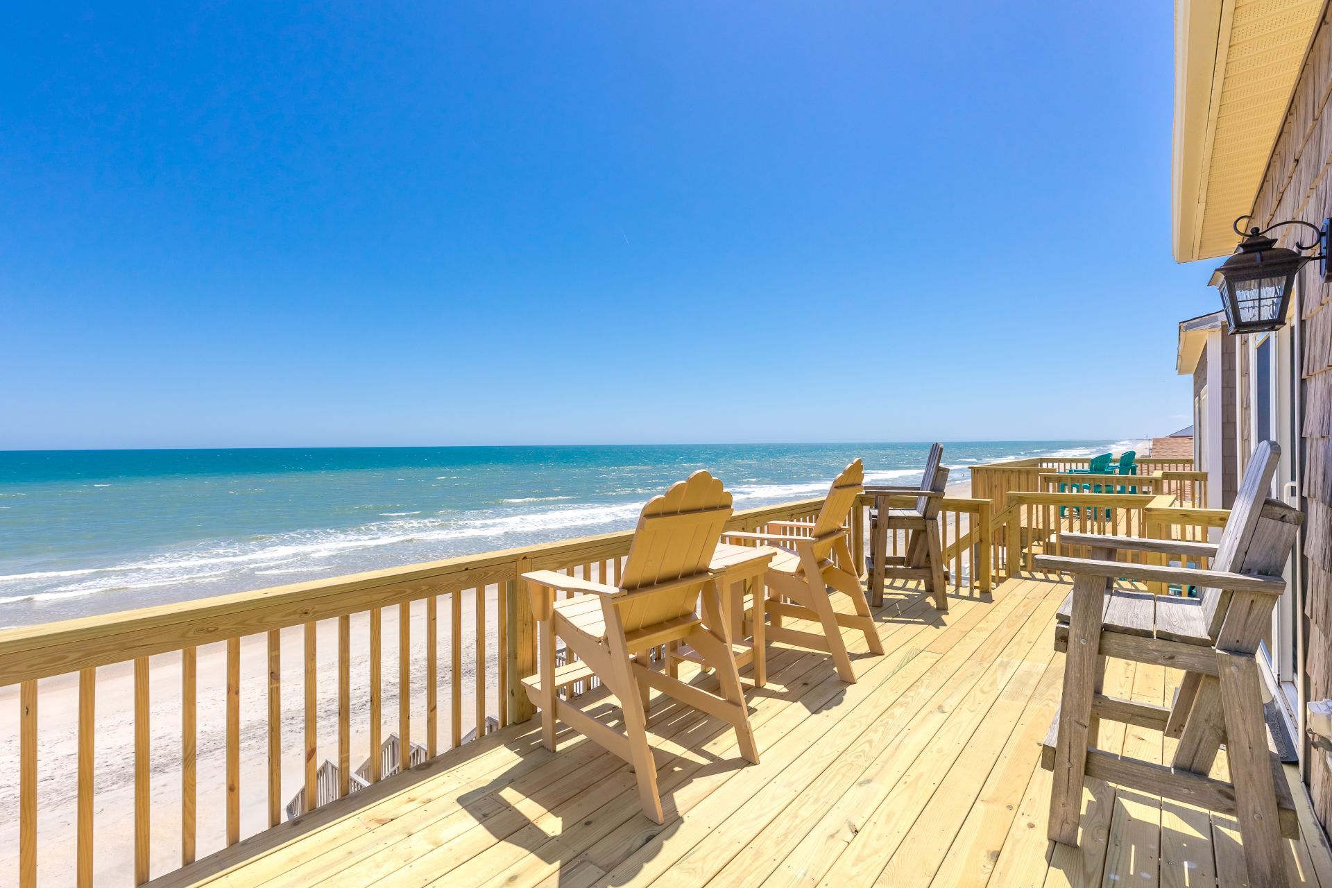 A wooden deck with chairs overlooking a beach.