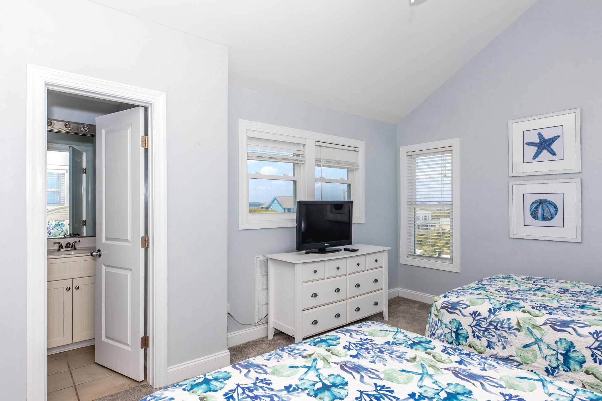 A bedroom with a TV, dresser, two beds, and a door leading to a bathroom.