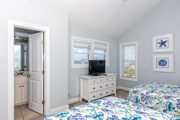 A bedroom with a TV, dresser, two beds, and a door leading to a bathroom.