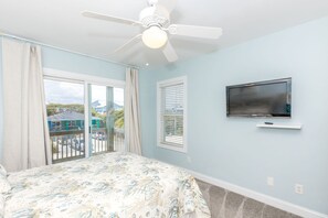 A bedroom with a bed, a ceiling fan, a TV, and a view of the outside.