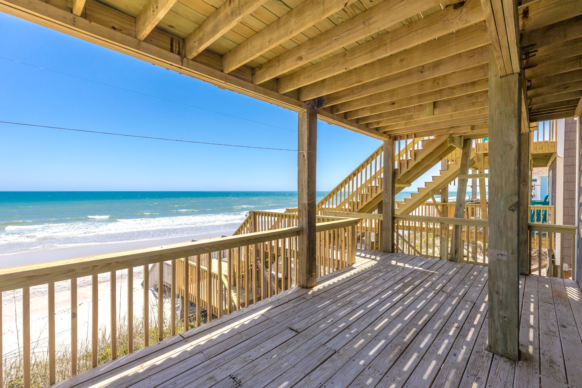 A wooden deck with a view of the beach and ocean.