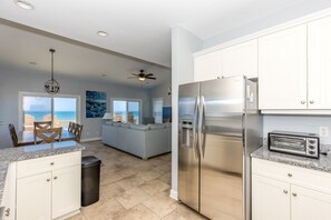 A modern kitchen with a stainless steel refrigerator, granite countertops, and a view of the ocean.