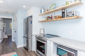 A modern kitchen with stainless steel appliances, wooden shelves, and a striped rug.