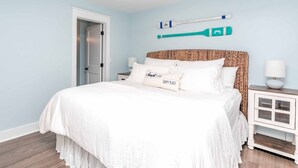 A bedroom with a bed, pillows, a nightstand, a lamp, and a door. - Shoreside Cottage - Classic 2 BR Beauty - Amazing Views from Covered Porch! Dog (Surf City)