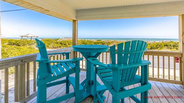 A covered deck with two turquoise Adirondack chairs and a small round table, overlooking a beach and ocean. - Shoreside Cottage - Classic 2 BR Beauty - Amazing Views from Covered Porch! Dog (Surf City)